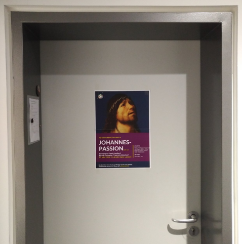 foto einer grauen bürotür, auf der ein plakat für eine aufführung der johannes-passion befestigt ist