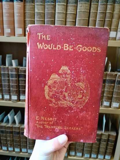 Holding an old edition of Edith Nesbit's The Would-Be-Goods in front of other vintage tomes