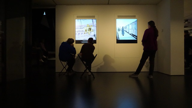 Drei Personen hören sich Inhalte einer Ausstellung an, zwei sitzen.