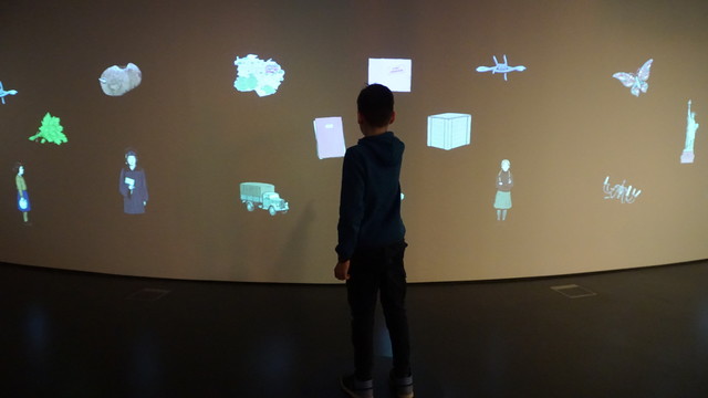 Ein Junge vor einer Wand. Auf die Wand sind Gegenstände projiziert.