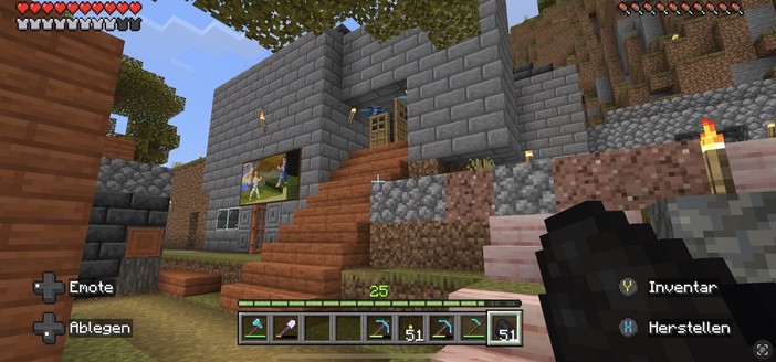 A screenshot from the game Minecraft showing a player's perspective with a health bar on top, an inventory bar at the bottom, and the game's environment consisting of a stone house with wooden stairs, torches, and trees.