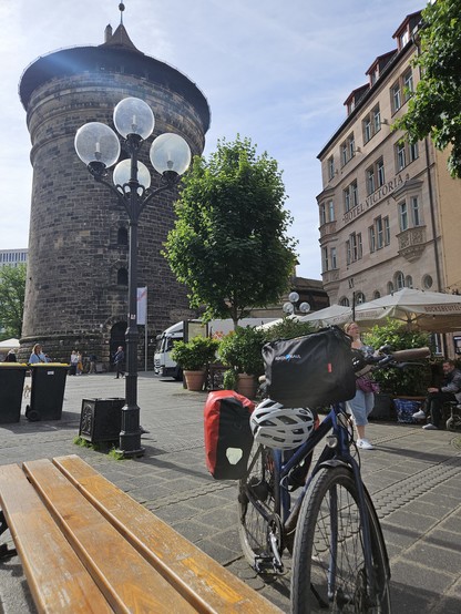 Mein Fahrrad steht bepackt mit Radtaschen vor einem historischen Turm in Nürnberg. Der Himmel ist blau.