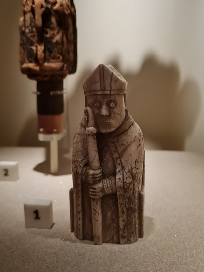 Ein einsamer Lewis Chessmen aus Elfenbein steht in einer Vitrine, neben ihm ist eine kleine 1 aufgestellt. 