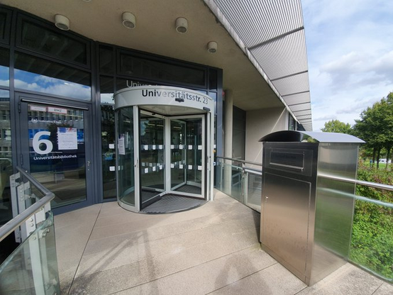 Eingang zur UB, man sieht die Bücherbox vorm Eingang, die Drehtür sowie die Automatiktür links daneben. 