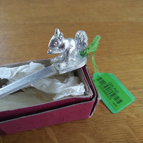 foto eines ausschnitts eines silberfarbenen metall-brieföffners, an dessen ende eine kleine eichhörnchen-figur sitzt, auf der roten pappkarton-verpackung und noch mit dem 