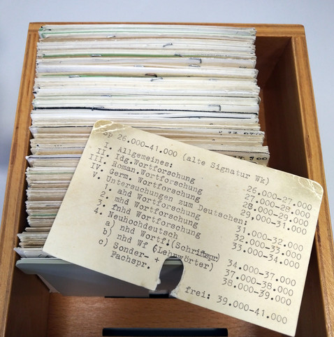 foto eines holzkastens mit alten bibliothekskatalogkarten, darauf eine übersichtskarte mit signaturenbereichen für namenskundliche literatur