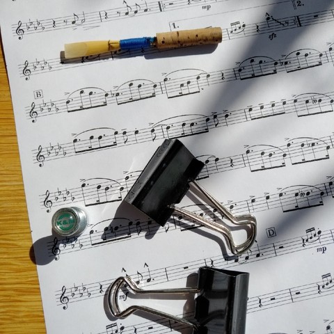 foto einer notenseite eines orchesterstückes in des-dur, darauf verteilt ein oboen-rohr, zwei maulklemmen und ein kleiner magnet