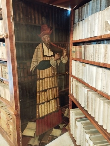 Holzbemalung in einem Regal einer historischen Bibliothek, die einen aus Büchern bestehenden Mann darstellt.