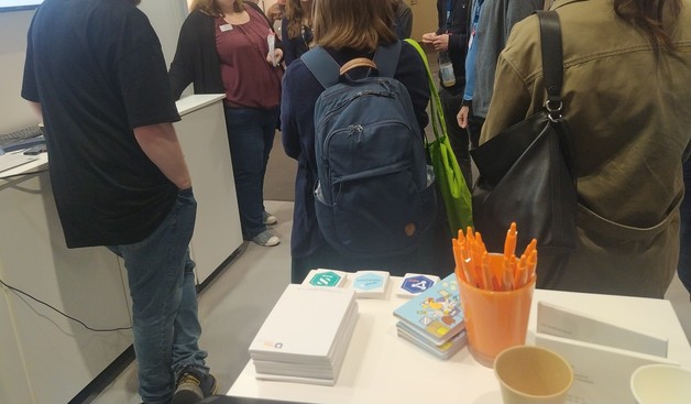 Foto vom hbz-"Stand" mit dem beschriebenen Merch und einer Gruppe Menschen davor.