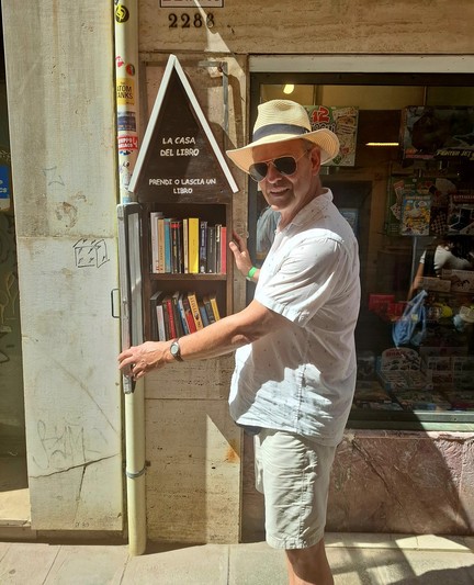 Mann mit Hut und Sonnenbrille vor einem Bücherregal.