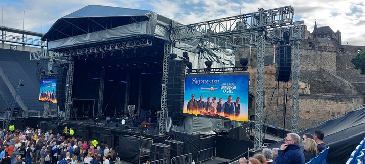 A photo of the stage set up on the Esplanade in front of Edinburgh Castle. On both side of the stage screens announcing the 25th anniversary concert of Skipinnish.