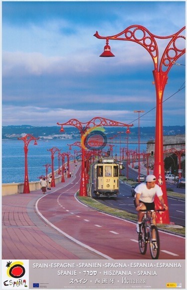 Ein Küstenweg mit einem Radfahrer im Vordergrund und einer Straßenbahn im Hintergrund. Der Weg ist von verzierten roten Straßenlaternen gesäumt. Verschiedene Sprachen am unteren Rand buchstabieren 
