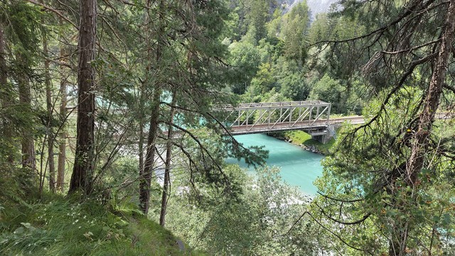 Blick von einem Berg hinab auf eine Fluss und eine Eisenbahnbrücke. Der Fluss ist türkis-blau, die Brücke aus Metall.