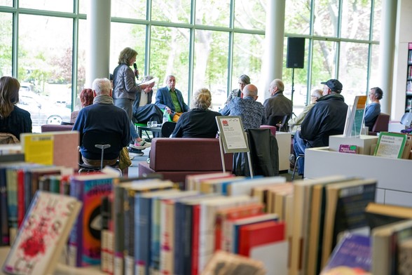 Foto: Blick in eine Bibliothek, in der verschiedene Menschen bei einer Podiumsdiskussion sitzen und diskutieren.