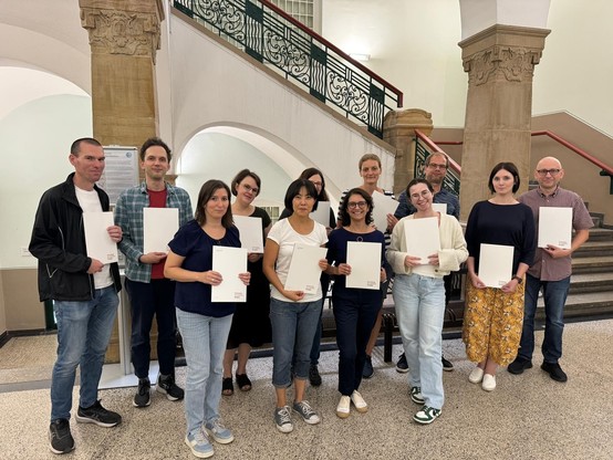 Gruppenfoto der Absolvent*innen mit ihren Zertifikaten in den Händen