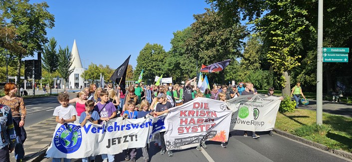 Front der Klimademo am Bahnhof Göttingen. Banner sind zu sehen: u a : Verkehrswege jetzt! Und: Die Krisen haben System. Der Himmel ist strahlend blau. 