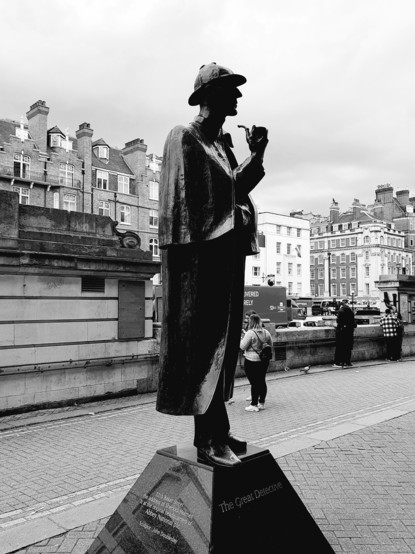 Statue of Sherlock Holmes, 'The Great Detective', in London. Black and white image shows the iconic figure with pipe against a backdrop of classic British architecture.