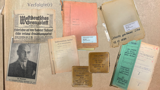 In der linken Bildhälte zu sehen ein Zeitungsbild des von den Nationalsozialisten abgesetzten Aachener Oberbürgermeisters Wilhelm Rombach (1884-1973), ein zeitgenössischer Artikel sowie eine Akte zum Fall. In der rechten Bildhälfte Stolpfersteine und Akten zur Verfolgung der Familie Levano aus Aachen.
