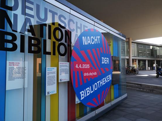 Außenvitrine der Deutschen Nationalbibliothek Frankfurt. Ein großer runder Aufkleber mit blauen und roten Strahlen mit der Aufschrift Nacht der Bibliotheken, 4.4.2025.