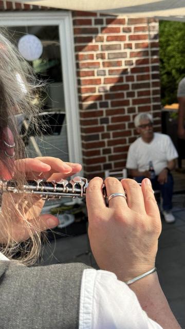 foto einer person, die eine piccolo-flöte spielt, von hinten fotografiert, sodass man nur die hände und die flöte sieht
