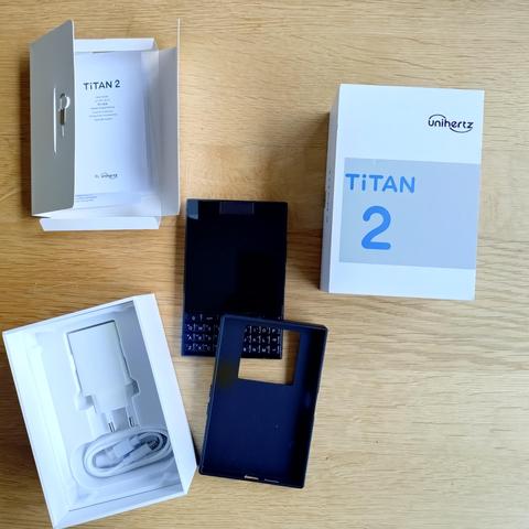 foto des smartphones titan 2 von unihertz auf einem holztisch mit einer schutzhülle und der verpackung
