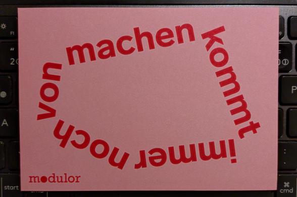 eine hellpinkfarbene postkarte von der firma modulor mit dem "machen"-zitat als kreis geschrieben