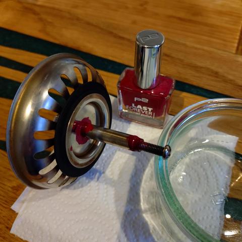 foto eines küchenspülenabflusseinsatzsiebes von unten, um dessen schraube an zwei stellen pinkfarbener nagellack gepinselt wurde, abgestützt von einem weck-glas; im hintergrund ist das nagellackfläschchen zu sehen