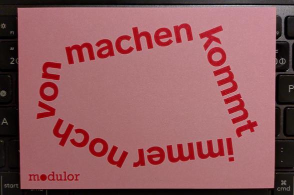 eine hellpinkfarbene postkarte von der firma modulor mit dem "machen"-zitat als kreis geschrieben