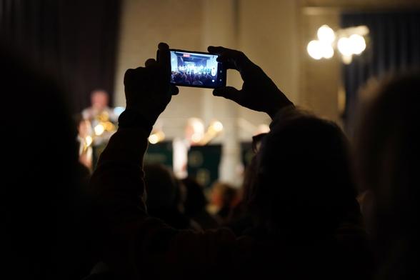 foto eines hochgehaltenen handys, mit dem jemand das orchester fotografiert