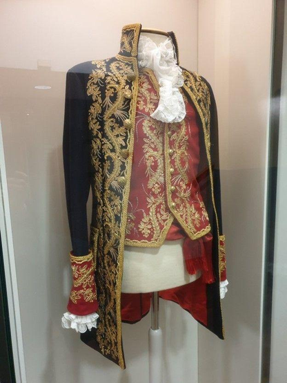 In einer Museumsvitrine ist auf einem Ständer höfische Oberbekleidung für Herren ausgestellt, bestehend aus Spitzenhemd, roter, goldbestickter Weste und schwarzem, goldbestickten Uniformrock. Man sieht auch einen schalartigen, roten geschlungenen Gürtel, die Hose, vermutlich eine Culotte, fehlt.