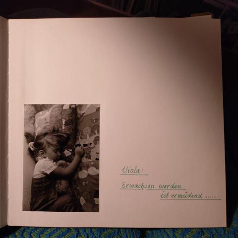 foto einer seite aus einem fotoalbum: links das bild eines schlafenden kleinen kindes, rechts ein handschriftlicher spruch: "viola: erwachsen werden ist ermüdend ..." 