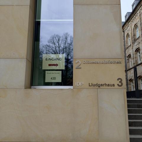 foto einer ecke des gebäudes der diözesanbibliothek in münster; in einem fenster hängt unter einem schild "eingang" mit einem pfeil nach rechts" ein schild mit der information "anzahl der fenster: 420"
