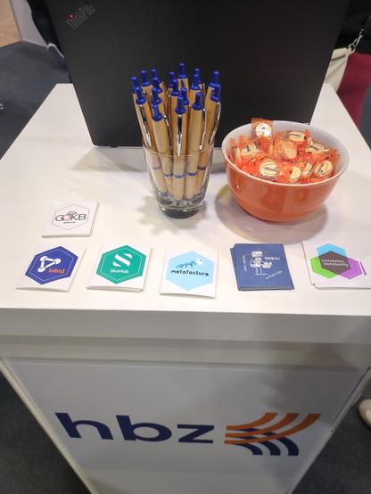 hbz Stand mit GoKB-, lobid-, SkoHub-, Metafacture-, SWIB-, und metadaten.community-Stickern und hbz-Kugelschreibern.