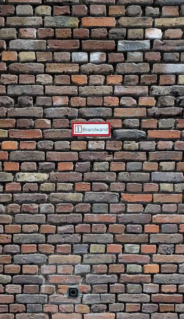Eine Ziegelwand mit einem Schild auf dem Brandwand steht.