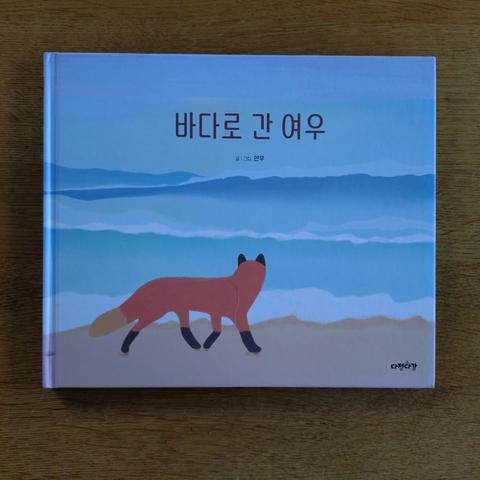 foto des buches "바다로 간 여우", "der fuchs, der ans meer ging": man sieht einen fuchs von hinten, der an einem strand entlangläuft und aufs wasser schaut