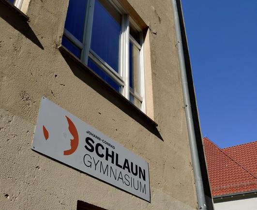 foto eines schildes mit dem schul-namen am gebäude des johann-conrad-schlaun-gymnasiums in münster; am rechten bildrand sieht man einen strahlend blauen himmel