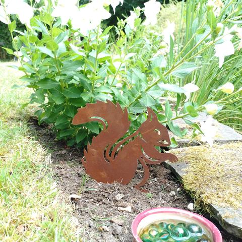 fotos eines blumenbeetes, in dem eine flache eichhörnchen-figur setzt, hinter einer schale mit murmeln und wasser