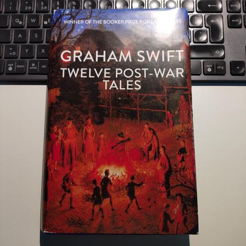 foto des buches "twelve post-war tales" von graham swift in der hardcover-ausgabe auf einem weißen schreibtisch, halb auf einer schwarzen computertastatur liegend