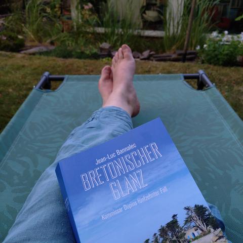 foto einer liege in einem garten mit einem paar füße und dem buch "bretonischer glanz – kommissar dupins fünfzehnter fall"