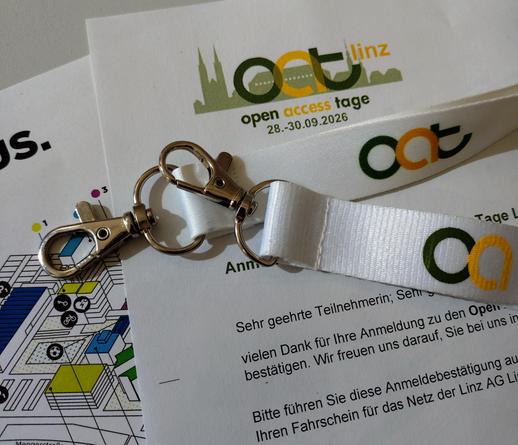 foto zweiter lanyards mit dem logo der open-access-tage auf einer anmeldebestätigung für die tagung 2026 und einem campusplan der uni linz