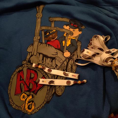 foto der rückseite einer blauen hoodie-jacke mit einer zeichnung der lokomotive aus "jim knopf und die wilde 13" mit dem schriftzug "abi 96" vorne auf der lok, darauf weiße armbände mit der zeichnung in klein und den jahreszahlen 1996 und 2026