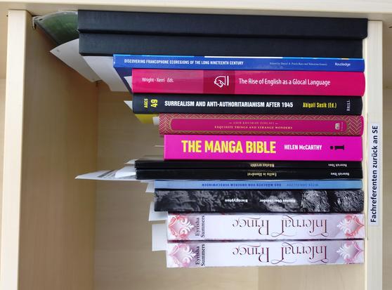 foto einiger bücher in einem regalfach; zu besseren lesbarkeit der titel auf den buchrücken wurde das foto um 90 grad nach links gedreht