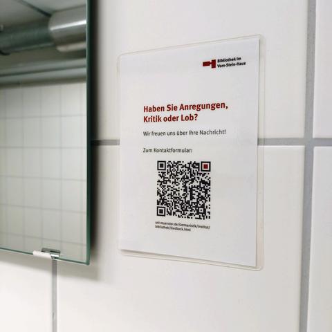 foto eines kleinen schildes mit der bitte um feedback zu einer bibliothek mit einem QR-code und der URL zum formular